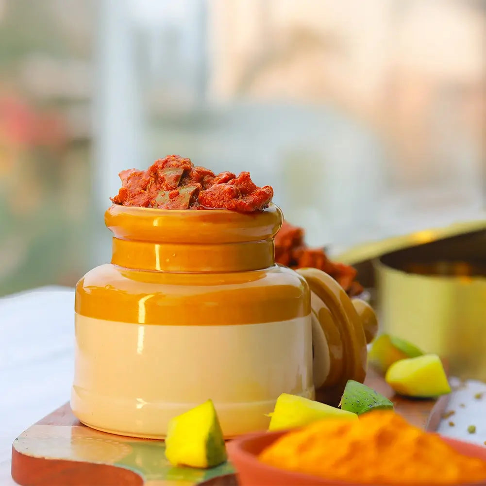 Yellow ceramic jar with mango pickle on a wooden surface with blurred background