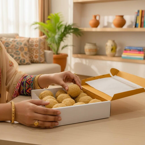 Person in a traditional outfit reaching into a box of laddus in a home setting