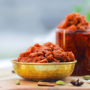 Chicken pickle in a gold bowl on a wooden surface with spices in the background.