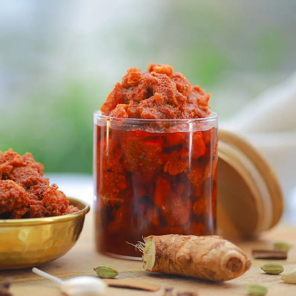 Glass jar and bowl filled with chicken pickle on a wooden surface with a blurred natural background