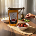 Traditional pickle being scooped from a bowl with a package labeled 'Traditional Pickles & Podi' on a wooden table.