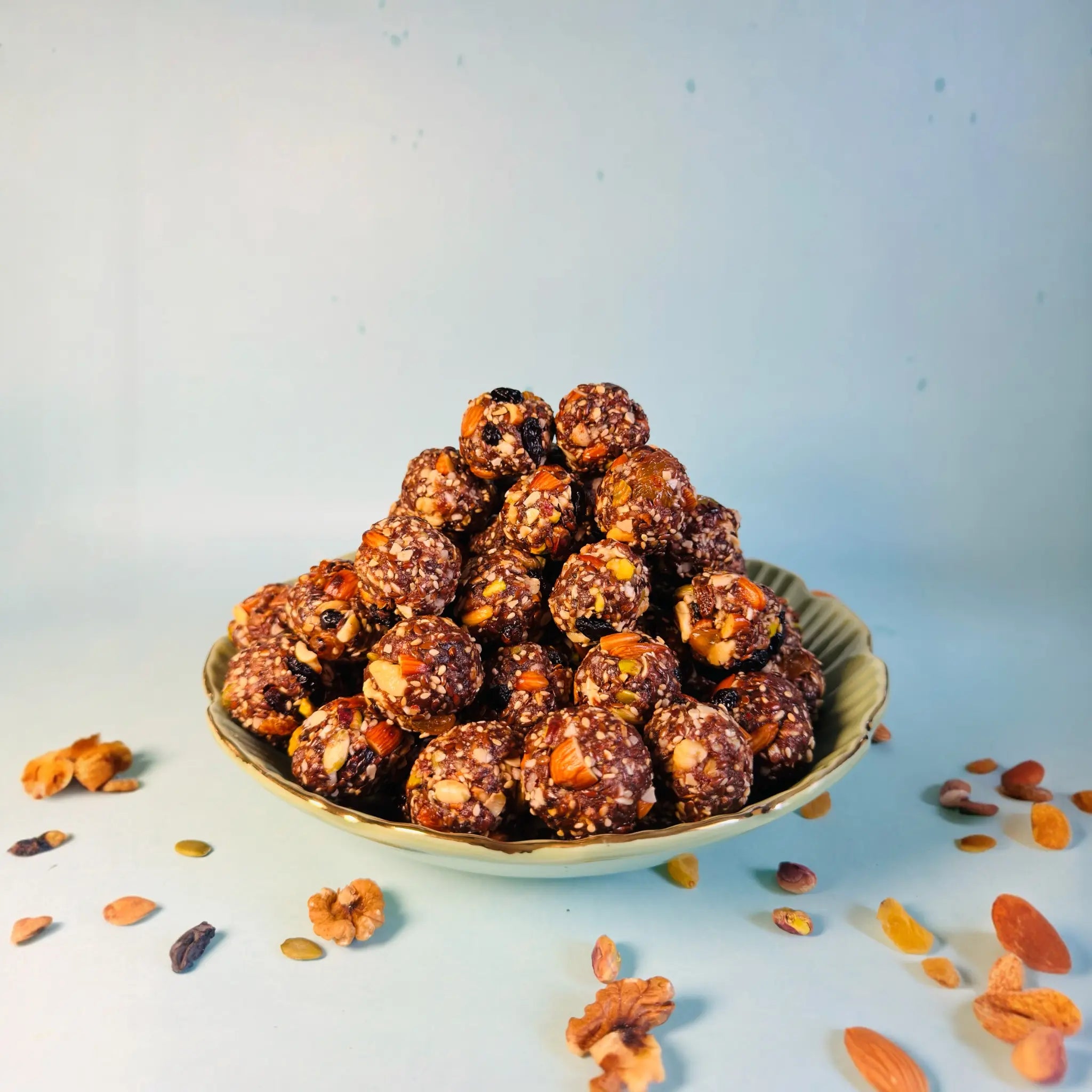 Bowl of dry fruit laddu with nuts on a light blue background