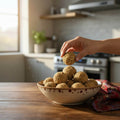 Hand picking a gond laddu from the bowl on a kitchen counter