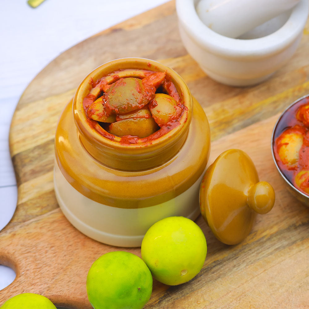 Jar of Lemon pickle on a wooden board with limes and a mortar and pestle.