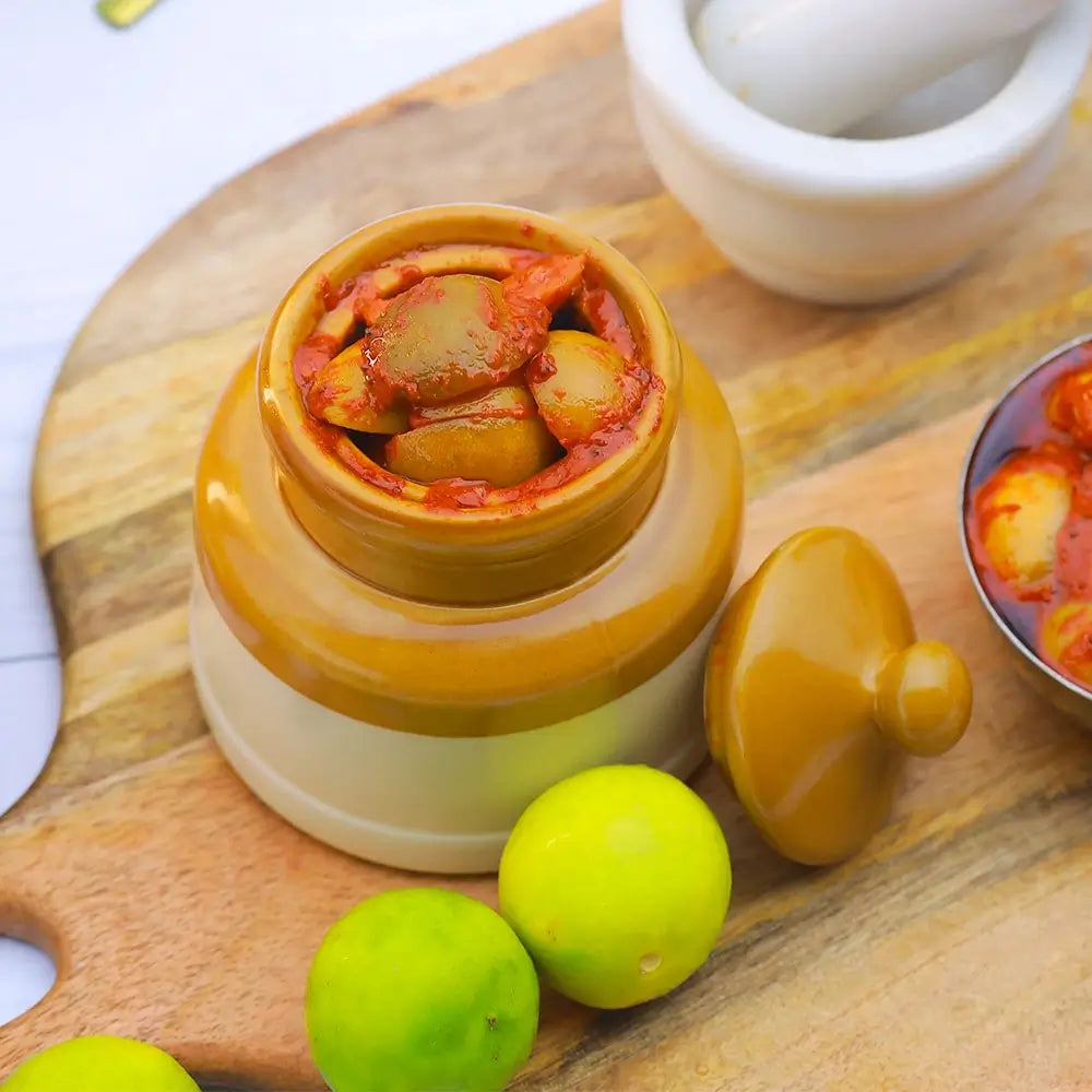 Jar of lemon pickle on a wooden board with limes and a mortar and pestle.