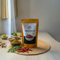 Yellow package of 'Karivepaku karam podi' on a wooden surface with spices and herbs.