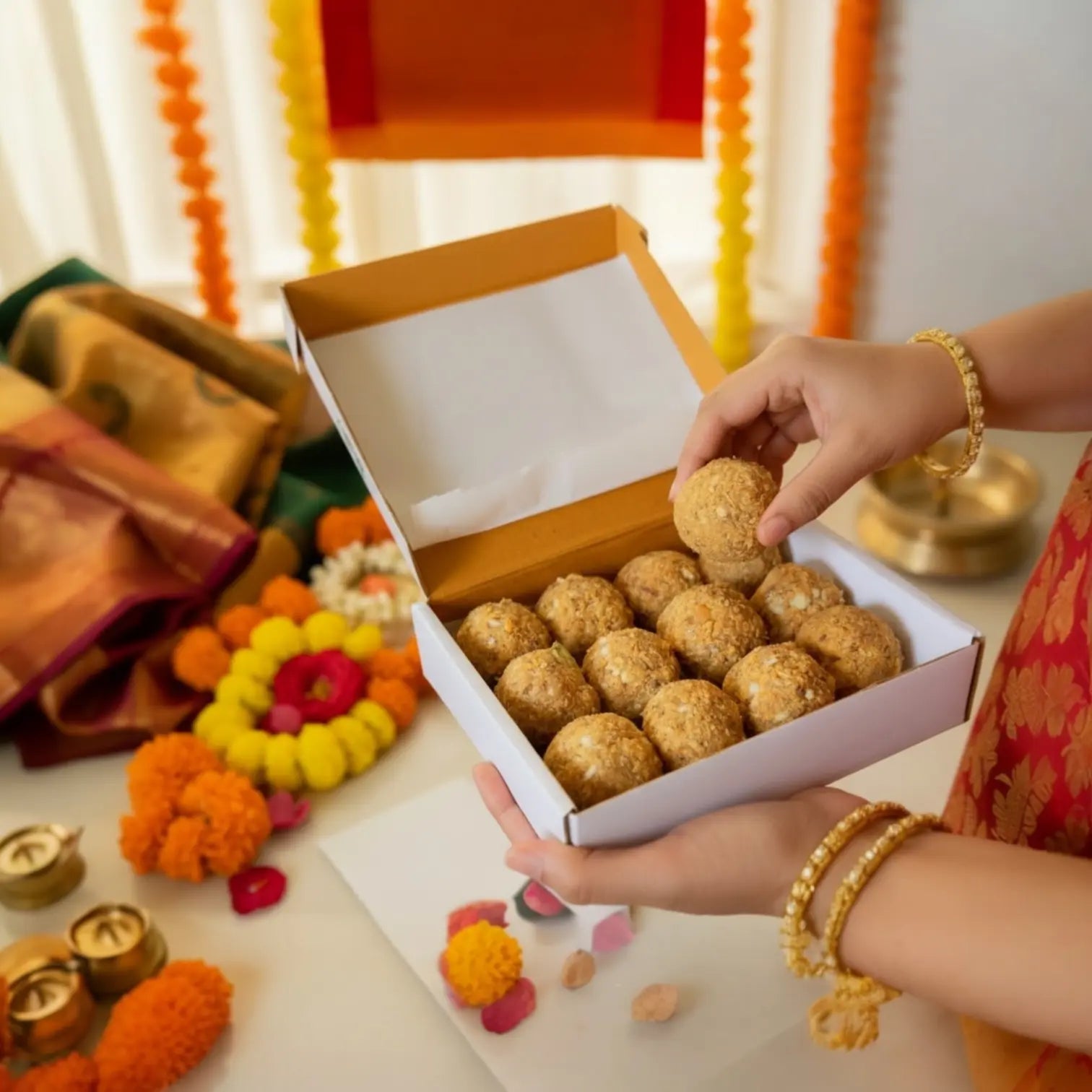 Person holding a box of traditional sweets with festive decorations in the background