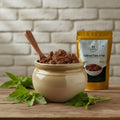 Jar of traditional mutton pickle with a wooden spoon and packaging on a wooden surface with a brick wall background.