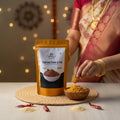 Packaging of nuvvula karam podi with a person in traditional attire in the background.
