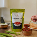 Green packet of  mulakkada pickle with a bowl of pickle and drumsticks on a wooden surface.