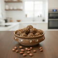 Bowl of palli laddus on a wooden table with a blurred kitchen background