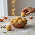 Hand picking a sunnunda from a terracotta bowl on a wooden surface with decorative lights in the background.