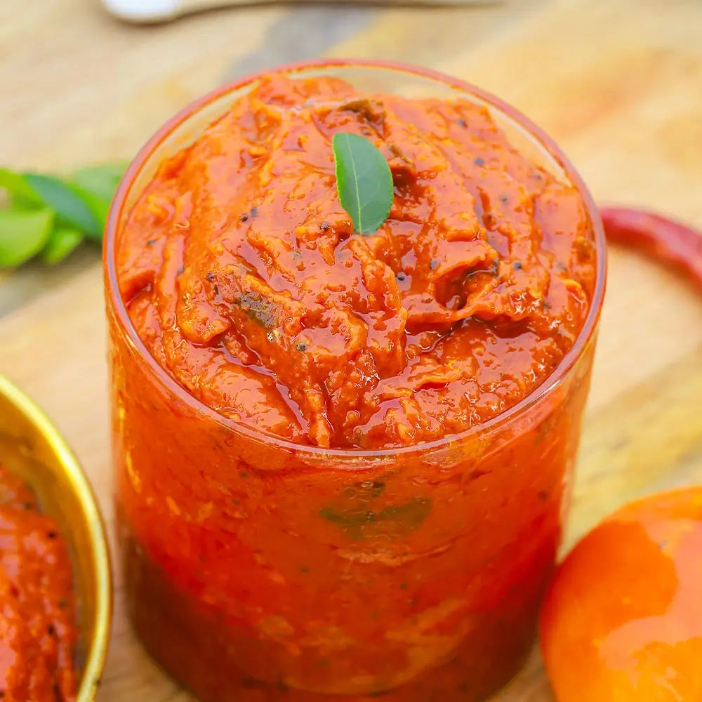 Close up shot of tomato pickle in a glass jar on a wooden surface with a leaf garnish.